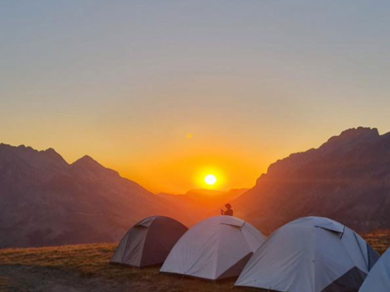 Bivouac en montagne près de Megève, avec une tente installée au sommet et une vue panoramique sur les Alpes au coucher du soleil.